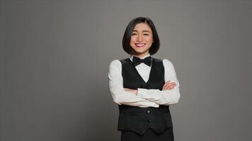 asiático mujer hotel conserje vistiendo elegante uniforme con arco, trabajando en hospitalidad industria como un recepcionista. recepción escritorio administrador saludo clientela, gris antecedentes. cámara una. foto