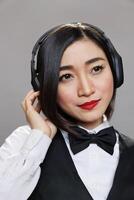 Beautiful asian waitress enjoying song playlist in headphones closeup. Young attractive woman receptionist wearing black and white uniform listening to music in earphones photo