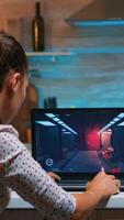 Young woman gamer playing online professional game on laptop at home late at night. Professional player testing online video games on her personal computer with modern technology network wireless. photo