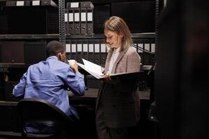 Workers discussing management report, analyzing administrative documents in corporate depository. Diverse employees reading bureaucracy record, discovering accountancy files in storage room photo