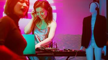 Smiling girl mixing music at DJ station, creating cheerful atmosphere at club on stage. Happy modern woman having fun with sounds at audio panel, clubbing with friends on dance floor. photo