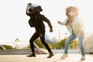 joven afro amigos bailando al aire libre mientras escuchando a música con inalámbrico auriculares y Clásico boombox foto