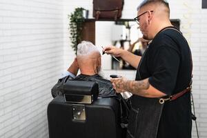 Male hairdresser cutting hair to beard senior client - Young hairstylist working in barbershop - Health care and haircut salon concept photo