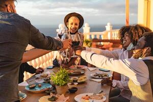 Young friends toasting with red wine glasses at dinner appetizer during sunset time - Drink and food concept photo