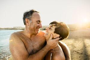 Happy senior couple having a romantic moment on the beach at sunset during summer vacations - Elderly people relationship concept photo