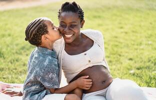 Happy African pregnant mother with son having tender moment in the park - Family love concept photo