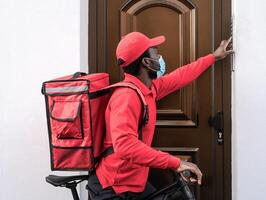 African rider man delivering meal to customers home with electric bicycle while wearing face mask during corona virus outbreak - Ecological fast delivery food concept photo