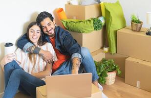 contento joven Pareja Moviente en nuevo hogar primero hora - hombre y mujer teniendo divertido utilizando computadora siguiente caja de cartón caja en nuevo propiedad casa - cambio Departamento día y personas estilo de vida relación concepto foto