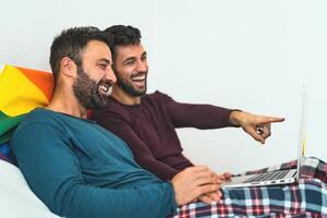 Happy gay men couple using laptop in bed- Homosexual love and gender equality in relationship concept photo