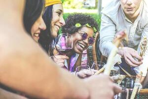 contento amigos haciendo un picnic en un parque al aire libre - joven personas disfrutando hora juntos Bebiendo rojo vino y comiendo un pan con jamón en el patio interior - concepto de amistad - atención en afro mujer foto