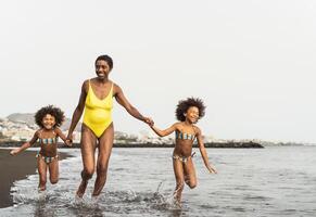 Happy Afro family having fun running on the beach during summer time - Parents vacations and travel lifestyle concept photo