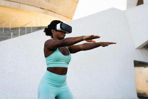 Happy fit African woman using futuristic virtual reality glasses during training session - Technology and Innovated workout concept photo