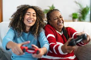 Happy mother and daughter having fun playing video game at home - Gaming entertainment and technology concept photo