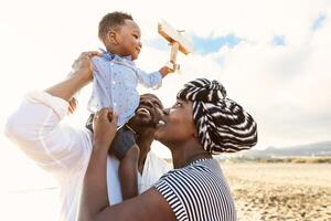 Happy African family having fun on the beach during summer vacation - Parents love and unity concept photo