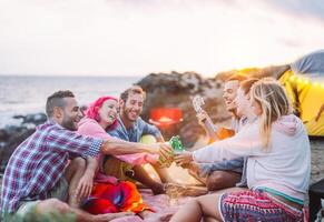 grupo de amigos aplausos con cervezas al aire libre - contento personas cámping con tienda y haciendo un parilla teniendo divertido tostado botellas de cerveza - amistad, estilo de vida, acampar concepto foto