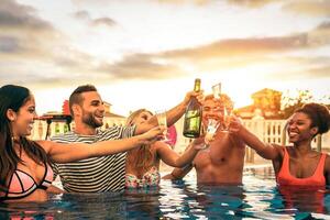 grupo de contento amigos haciendo un piscina fiesta aplausos con champán a puesta de sol - joven personas riendo y teniendo divertido tostado con espumoso vino en lujo tropical recurso - juventud estilo de vida concepto foto