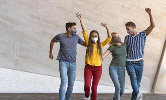 Young friends dancing together while wearing face mask outdoor - Happy people having fun in city after corona virus quarantine - Youth millennial generation friendship and health care concept photo