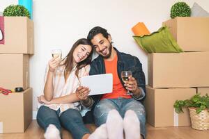 contento joven Pareja Moviente en nuevo propiedad casa - joven amantes teniendo divertido utilizando tableta compras en línea sentado siguiente caja de cartón caja - cambio Departamento día y personas estilo de vida relación concepto foto