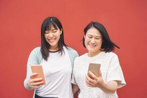 asiático madre y hija utilizando móvil teléfono inteligente al aire libre - contento chino familia teniendo divertido con nuevo tecnología de moda social medios de comunicación aplicaciones - tecnología adiccion estilo de vida personas concepto foto