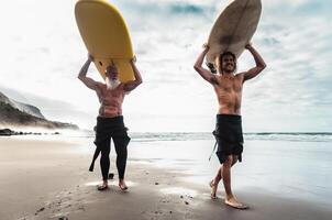 Happy friends surfing together on tropical ocean - Sporty people having fun during vacation surf day - Extreme sport lifestyle concept photo