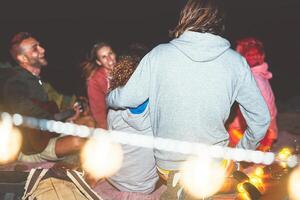 contento amigos teniendo divertido jugando guitarra en cámping con Clásico ligero siguiente el playa a noche al aire libre - milenario joven personas en cámping vacaciones Días festivos - amistad y juventud fiesta estilo de vida foto