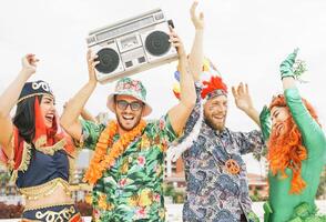 Happy friends celebrating carnival party outdoor - Young crazy people having fun wearing costumes listening music with vintage boombox stereo - Youth holidays culture lifestyle concept photo