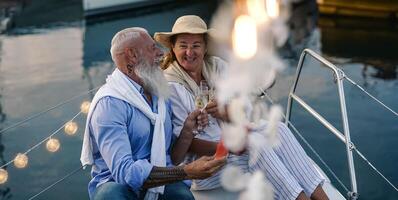 Senior couple toasting champagne and eating fruits on sailboat vacation - Happy elderly people having fun celebrating wedding anniversary on boat trip - Love relationship and travel lifestyle concept photo