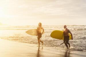 Happy friends with different age surfing together on tropical ocean - Sporty people having fun during vacation surf day - Elderly and youth people sport lifestyle concept photo