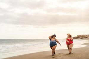 Happy plus size women having fun walking on the beach - Curvy confident people lifestyle concept photo