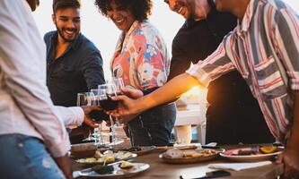 Young friends toasting with red wine at appetizer sunset time on patio house - Drink and food concept photo