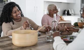 Happy afro Latin family eating healthy lunch with fresh vegetables at home - Food and parents unity concept photo