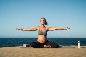 joven embarazada mujer haciendo yoga sesión siguiente el mar - meditación y maternidad concepto foto