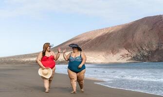 Happy plus size women having fun walking on the beach - Curvy confident people lifestyle concept photo
