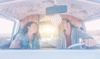 Happy couple driving a minivan and laughing while looking at each other - Young people having fun during a roadtrip on summer at sunset - Vintage filter - Vacation, travel, love concept photo