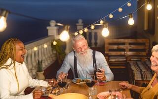 Happy multiracial senior friends having fun dining together on house patio - Elderly lifestyle people and food concept photo