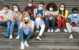 Young multiracial group of friends using mobile smartphone while wearing face mask during covid19 - Youth millennial lifestyle concept photo