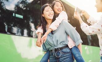 Happy Asian girls having fun outdoor - Millennial young people sharing time together and using mobile smartphone new trendy apps - Concept of friendship lifestyle with technology photo