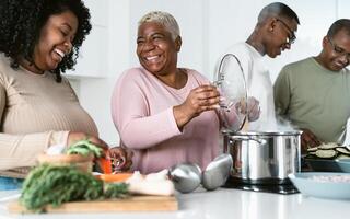 contento africano familia teniendo divertido en moderno cocina preparando comida receta con Fresco vegetales - comida y padres unidad concepto foto