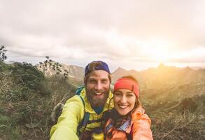 Happy couple taking selfie while doing trekking excursion on mountains - Young hikers having fun on exploration nature tour - Relationship and travel vacation lifestyle concept photo