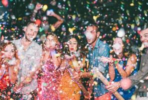 Happy friends doing party throwing confetti in the club - Millennials young people having fun celebrating in the nightclub - Nightlife, entertainment and festive holidays concept photo