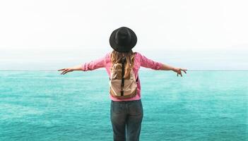 Young woman backpacker exploring new destinations - Back view of travel girl looking the ocean horizon - Tourism and youth people concept photo