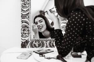 joven mujer aplicando maquillaje en frente de espejo - cosmético y estilo de vida personas concepto - negro y blanco edición foto