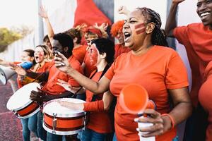 Crowd football fans exulting while watching soccer game at stadium - People with painted face and drum encouraging their team - Sport entertainment concept photo