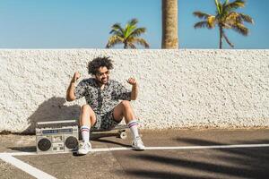 Young Afro Latin man having fun dancing while listening music with headphones and vintage boombox during summer vacations photo