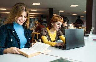 Young university students using laptop and reading book in library - School education concept photo