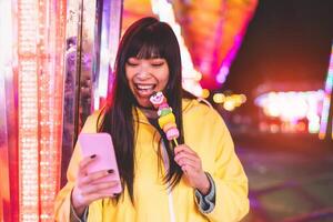 Asian girl taking using mobile phone in amusement park - Happy woman having fun with new trends smartphone apps - Youth millennial people generation and social media addiction concept photo