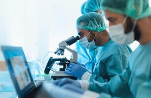 Doctors wearing personal protective equipment working in laboratory using computer and examining coronavirus through microscope - Science and technology concept photo