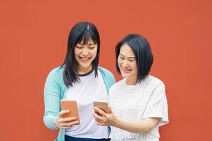 asiático madre y hija utilizando móvil teléfonos inteligentes al aire libre - contento chino familia teniendo divertido con nuevo tendencias tecnología aplicaciones para social medios de comunicación - social, tecnología y estilo de vida personas concepto foto