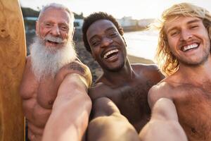 Happy fit surfers with different age and race taking selfie while having fun surfing together at sunset time - Extreme sport lifestyle and friendship concept photo