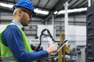 Engineer man working in robotic factory while monitoring the project on smart tablet - Tech industry concept photo